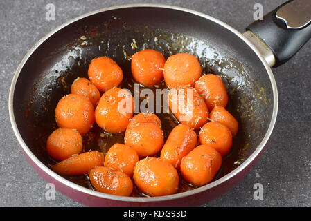 Glassato al miele carotine con sale marino e timo in una padella su un grigio Sfondo astratto. Il mangiare sano concetto. il digiuno cibo. pasto sano Foto Stock