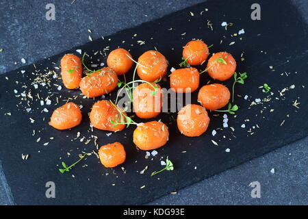 Glassato al miele carotine con sale marino e timo in un recipiente di metallo posto su un grigio Sfondo astratto. Il mangiare sano concetto. fissaggio di cibo. pasto sano Foto Stock