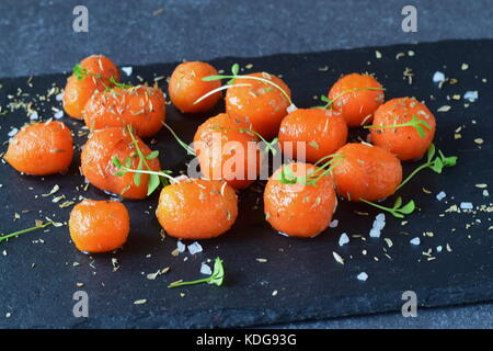 Glassato al miele carotine con sale marino e timo in un recipiente di metallo posto su un grigio Sfondo astratto. Il mangiare sano concetto. fissaggio di cibo. pasto sano Foto Stock