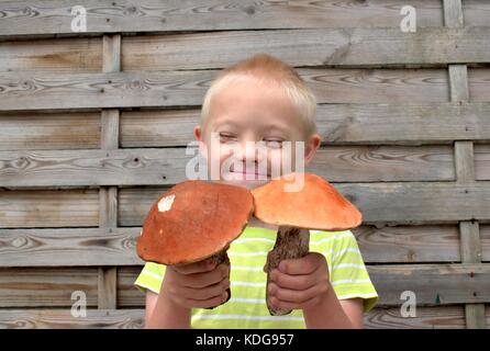 Felice ragazzo con la sindrome di down tenendo due grandi funghi. Foto Stock