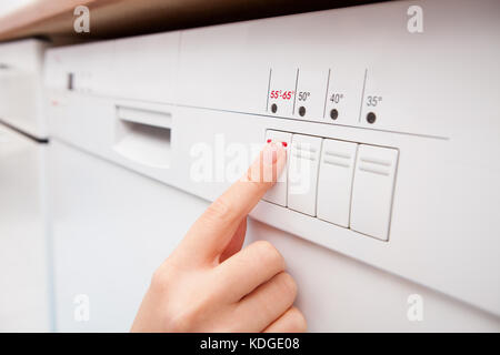 Close-up di donna di dito premendo il pulsante di lavastoviglie Foto Stock