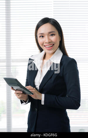 Sorridente imprenditrice asiatici in bright office utilizzando la calcolatrice Foto Stock