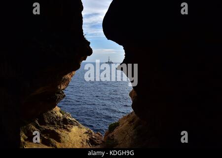 La vista dal mare grotta, formata attraverso agenti atmosferici / erosione della pietra calcarea maltese. L'uscita dalla grotta si affaccia sul mare con un impianto di trivellazione petrolifera nella distanza Foto Stock