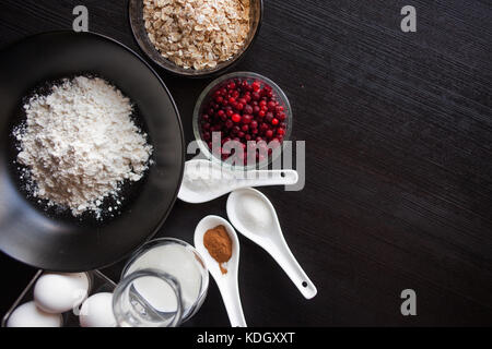 Farina, farina di avena, bacche, latte e uova, in piedi su un tavoli in legno nero Foto Stock
