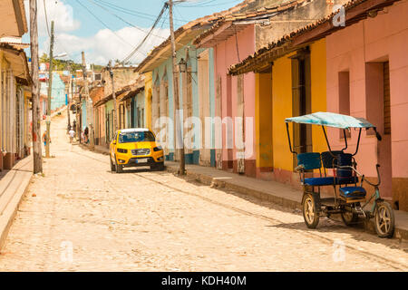 Scena di strada di un vecchio American automobile parcheggiata esterno colorato stile coloniale case sulla strada di ciottoli, Trinidad, Cuba, Caraibi, Foto Stock