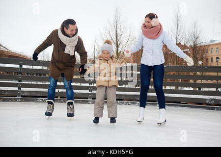 La famiglia contemporanea in azienda winterwear dalle mani mentre a pattinare sulla pista di pattinaggio sul ghiaccio Foto Stock