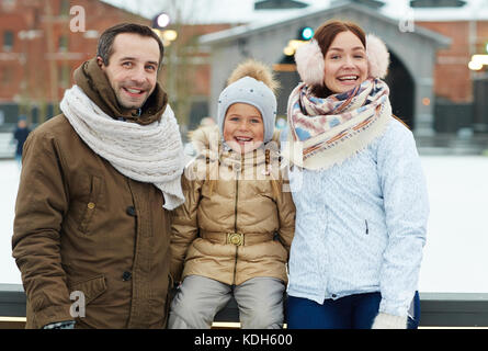 Allegro coppia giovane e carina la loro figlia in winterwear godendo weekend sulla pista di pattinaggio Foto Stock