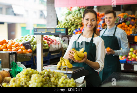 Sorridente giovane roba grembiuli in vendita banane dolce al marketplace Foto Stock