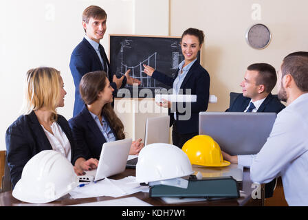 Ritratto di professionisti di successo con i caschi e laptop avente riuniti in ambienti interni Foto Stock