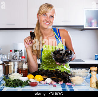 Sorridente giovane casalinga che prepara le vongole in acqua dolce in ambienti interni Foto Stock