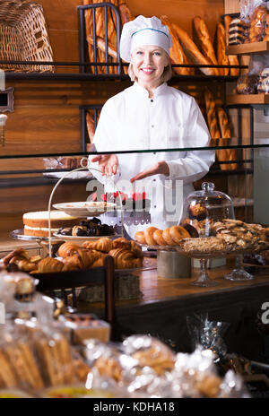 Donna matura offrendo fantasia e torte a base di pan di spagna per la vendita in cafe Foto Stock