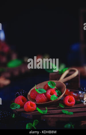 Frutti di bosco assortiti in una serva piatto di legno. lampone e blackberry con verde menta foglie scure della fotografia di cibo con copia spazio. Foto Stock