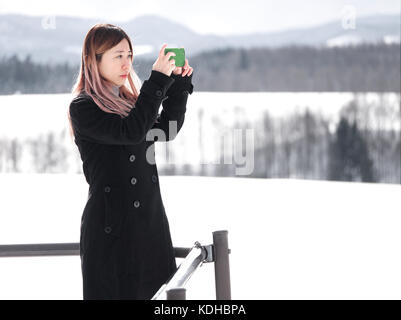 Asian Chinese Tourist scattare foto con un cellulare fotocamera a Biei, Hokkaido, Giappone, in inverno Foto Stock