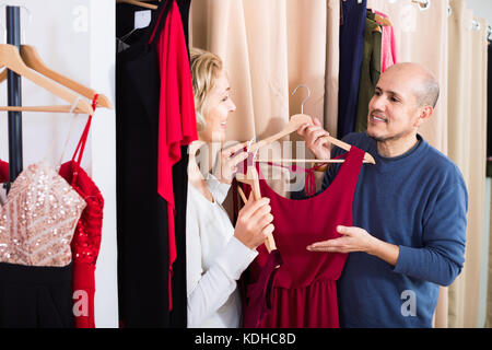 Donna sorridente medicazione in changeroom del negozio di abbigliamento, marito in attesa Foto Stock