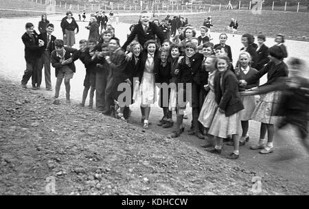 Anni sessanta, storico in questa immagine possiamo vedere un gruppo di inglese scuola secondaria i bambini e i ragazzi - alcuni indossano shorts - e le ragazze, ridendo e divertirsi insieme accanto a una ruvida ghiaia area esterna, Inghilterra. Foto Stock