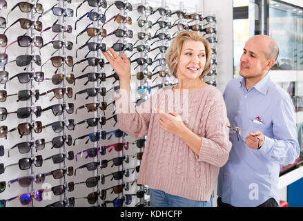 Senior russian giovane cercando montature per occhiali e sorridenti vicino stand Foto Stock