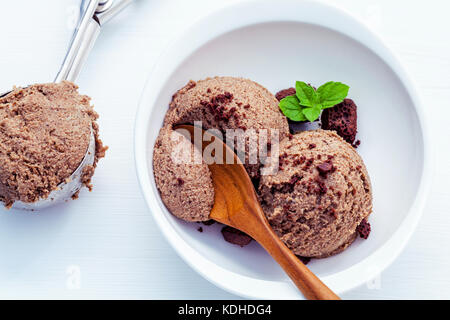 Close up di gelato al cioccolato in tazza bianca con fresche foglie di menta piperita e gelato scoop setup sul bianco sullo sfondo di legno . estate e dessert di me Foto Stock