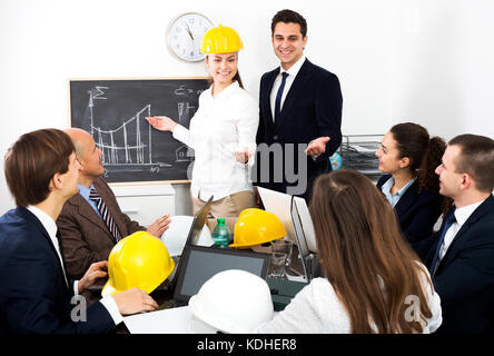 Professionisti di successo con i notebook e caschi con la presentazione del nuovo progetto in ufficio Foto Stock