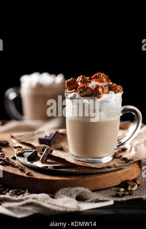 Composizione con due bicchiere di cappuccino la torta con panna montata e servite con i chicchi di caffè e cioccolato sul tagliere di legno sulla parte posteriore in nero Foto Stock