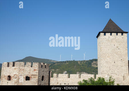 Il rumeno wind farm con turbina eolica e mulini a vento di fronte a un vecchio castello situato sulla parte serba del fiume Danubio, in cancelli di ferro valle. p Foto Stock