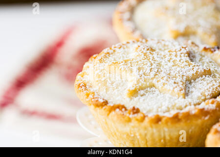 Tradizionale natale britannico pasticceria dolce cotto domestico pasticci di carne macinata con apple uvetta dadi sul riempimento bianco torta elegante piedistallo. golden frolla powd Foto Stock