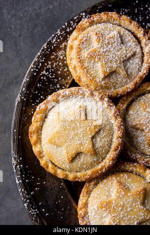 Tradizionale natale britannico pasticceria dolce cotto domestico pasticci di carne macinata con apple uvetta dadi riempimento frolla dorata in polvere vintage sulla piastra metallica d Foto Stock