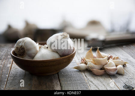 Teste d'aglio in un recipiente e chiodi di garofano sul tavolo di legno Foto Stock