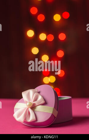 Scatola regalo rosa a forma di cuore aperto con bokeh sfocato sfondo luci colorate Foto Stock