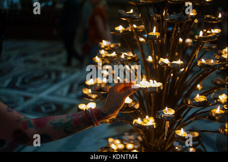Donna l'accensione di candele votive in una chiesa di Firenze, Italia Foto Stock