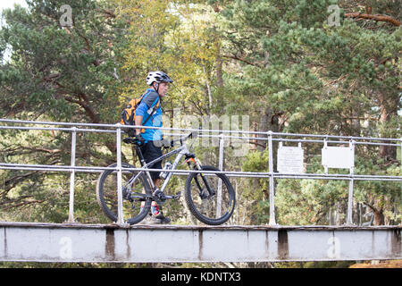 Un mountain biker ciclista tenendo la sua bicicletta come egli passa sopra la Cairngorm piedi ponte sulla via verso il Lairig Ghru mountain pass, Rothiemurchus Foto Stock