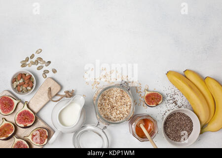 Ingredienti per la prima colazione: fiocchi d'avena, latte, fichi, banane, chia semi, miele, semi di zucca. vista da sopra Foto Stock