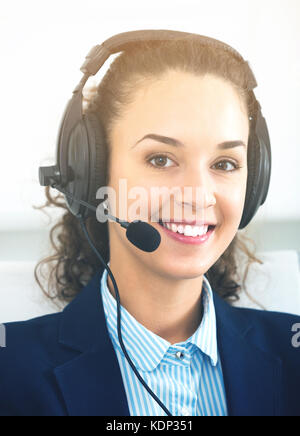 Ritratto di cordiale sorridente giovane donna con cuffia di risposta a una chiamata in ufficio Foto Stock