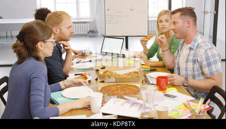 Giovani godendo la pizza in ufficio Foto Stock