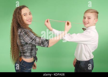 Ragazzo e ragazza stiramento da gomma da masticare che egli porta nella sua bocca isolati su sfondo verde Foto Stock