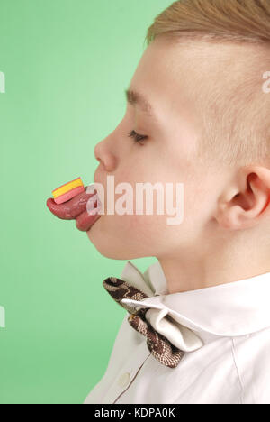 Ragazzo giovane mettere la gomma da masticare sulla sua linguetta isolata su sfondo verde Foto Stock