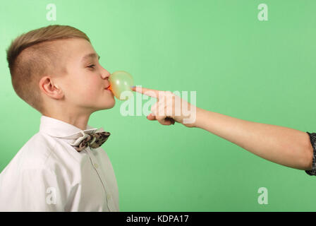 Ragazzo giovane stiramento da gomma da masticare che egli porta nella sua bocca isolati su sfondo verde Foto Stock