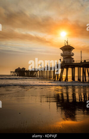 I fuochi selvatici locali pipelano fumo marrone dorato sopra i cieli del molo di Huntington Beach, creando paesaggi surreali. Foto Stock