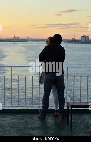 Una giovane coppia che abbraccia ogni altro su una barca in piedi a guardare il sole andare giù in un modo romantico con il tramonto come sfondo. Foto Stock