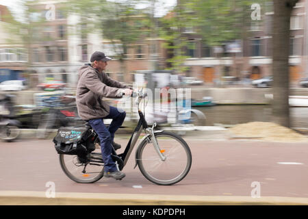 Un operaio di cicli attraverso la zona centrale di Amsterdam Foto Stock