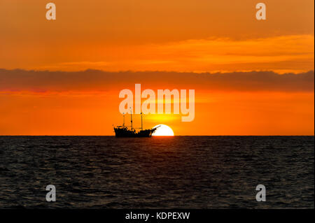 Nave Pirata silhouette è una nave pirata seduta sul mare guardando il tramonto sull'oceano stagliano contro il sole.. Foto Stock
