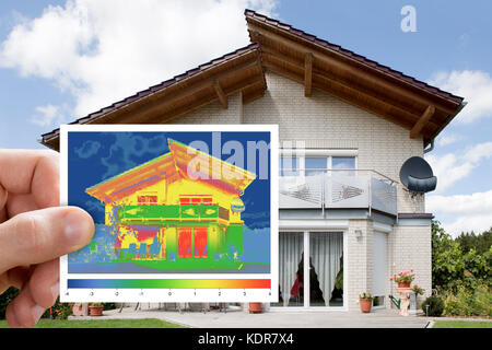 Persona Hand Holding termocamera a infrarossi immagine che mostra la mancanza di isolamento termico al di fuori della casa Foto Stock