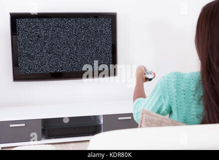 Donna seduta sul divano con telecomando guardando la televisione che non mostra alcun segnale Foto Stock