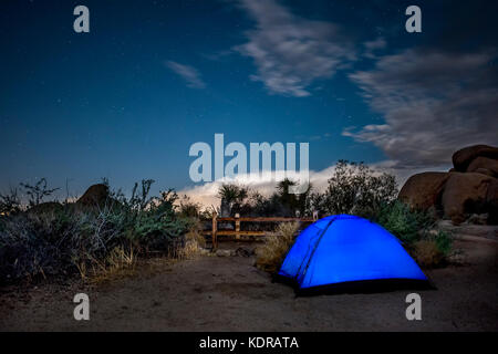 Un campeggio nel deserto del Mojave mostra una tenda blu illuminata mentre i campeggiatori si preparano a chiamarla una notte. Foto Stock