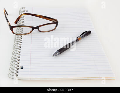 Notebook a spirale, marrone occhiali, e penna. Foto Stock