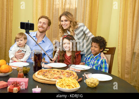 Famiglia tenendo selfie, tavolo da pranzo. Foto Stock