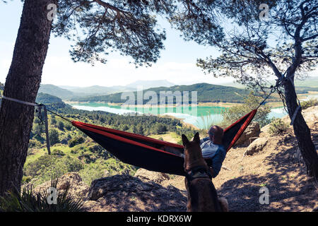 Wanderlust uomo e cane in un momento di relax a amaca in montagna. Foto Stock