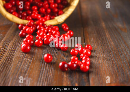 Cowberry, foxberry, cranberry, lingonberry sips dal cesto su un marrone tavolo in legno.