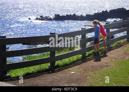 Un ragazzo e una ragazza guardando le onde in crash rocce laviche a Waianapanapa State Park, fuori l'Autostrada Hana, Maui, Hawaii Foto Stock