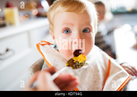 Simpatico bimbo seduto nel seggiolone mangiare. due bambini piccoli in una cucina. Foto Stock