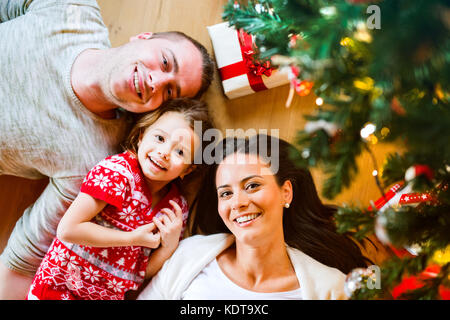 I giovani genitori con la loro piccola figlia sotto albero di natale che giace tra presenta. Foto Stock